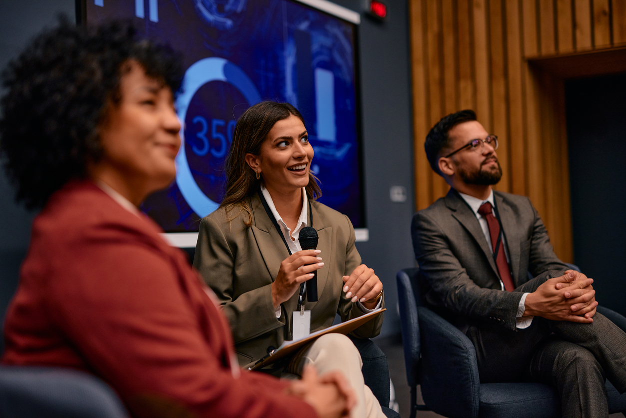 Businesswoman speaking at a conference using a microphone, sitting next to her colleagues stock photo