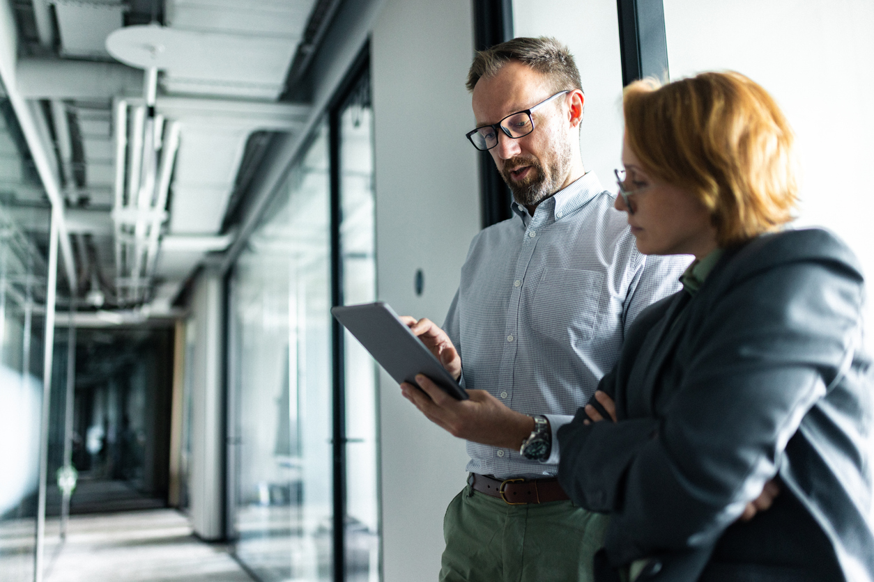 Two professionals discussing work in a modern office corridor setting