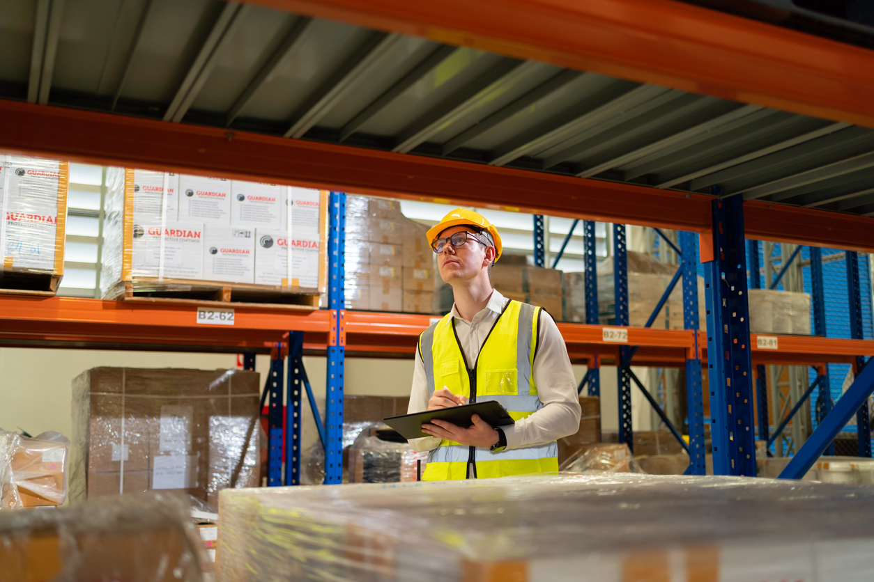 Warehouse worker holding tablet viewing inventory on shelves.